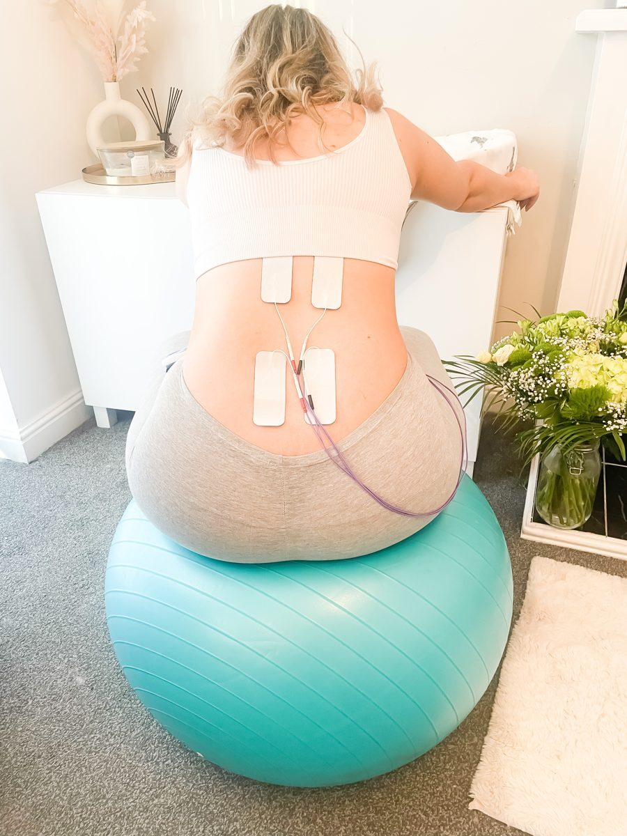 Pregnant woman sitting on a birthing ball with four TENS pads on her lower back